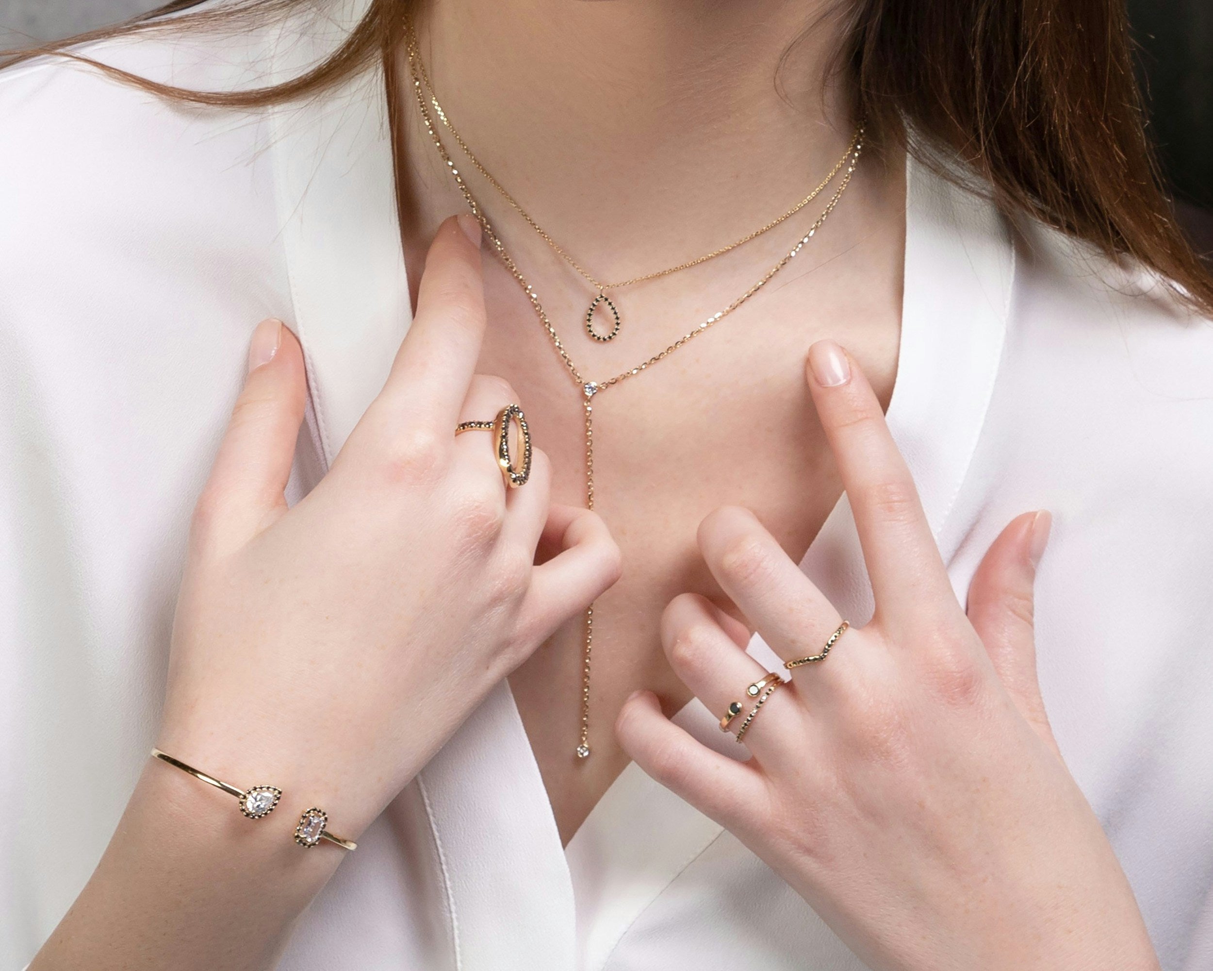 Close-up of a person wearing gold jewelry including a necklace, rings, and bracelet on a white background.